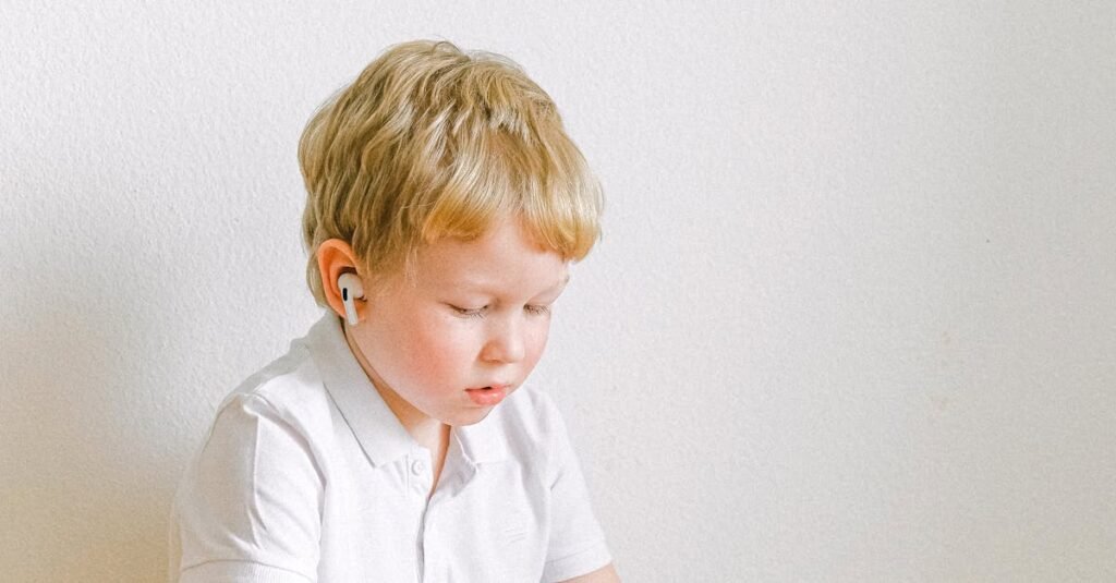A focused young boy using a tablet indoors, wearing earphones and seated cross-legged.