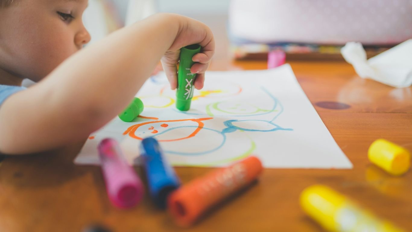 a little boy that is sitting at a table with some crayons